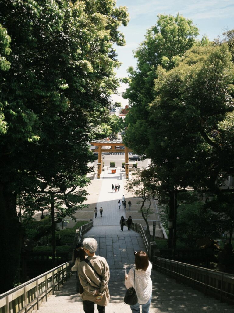 Two people descend steps toward a peaceful shrine under lush trees, capturing a serene outdoor setting.