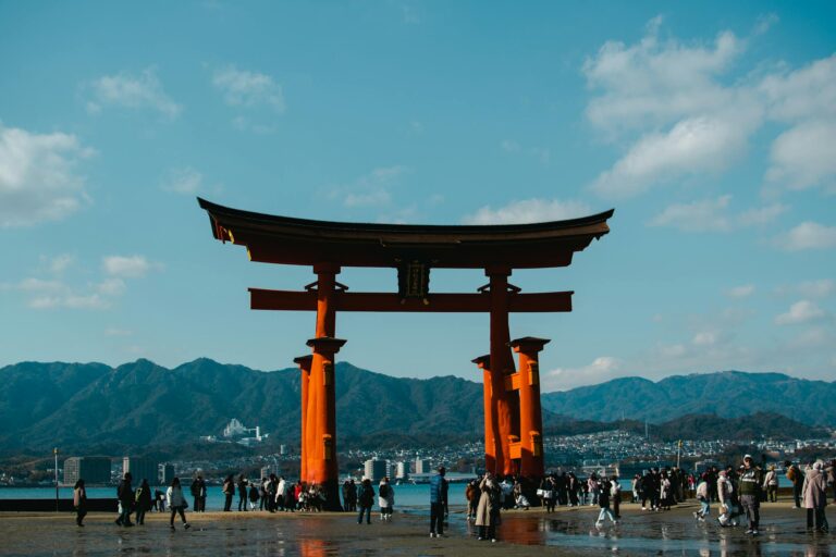 View of the famous Itsukushima Shrine Gate with tourists, set against mountains in Hiroshima, Japan.
