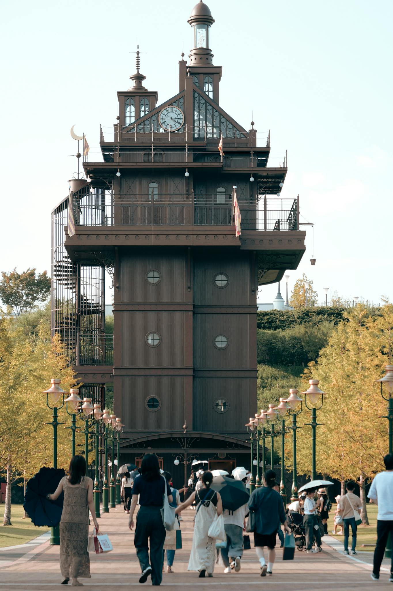 Visitors approaching the iconic clock tower at Ghibli Park, Nagoya, Japan during the day.